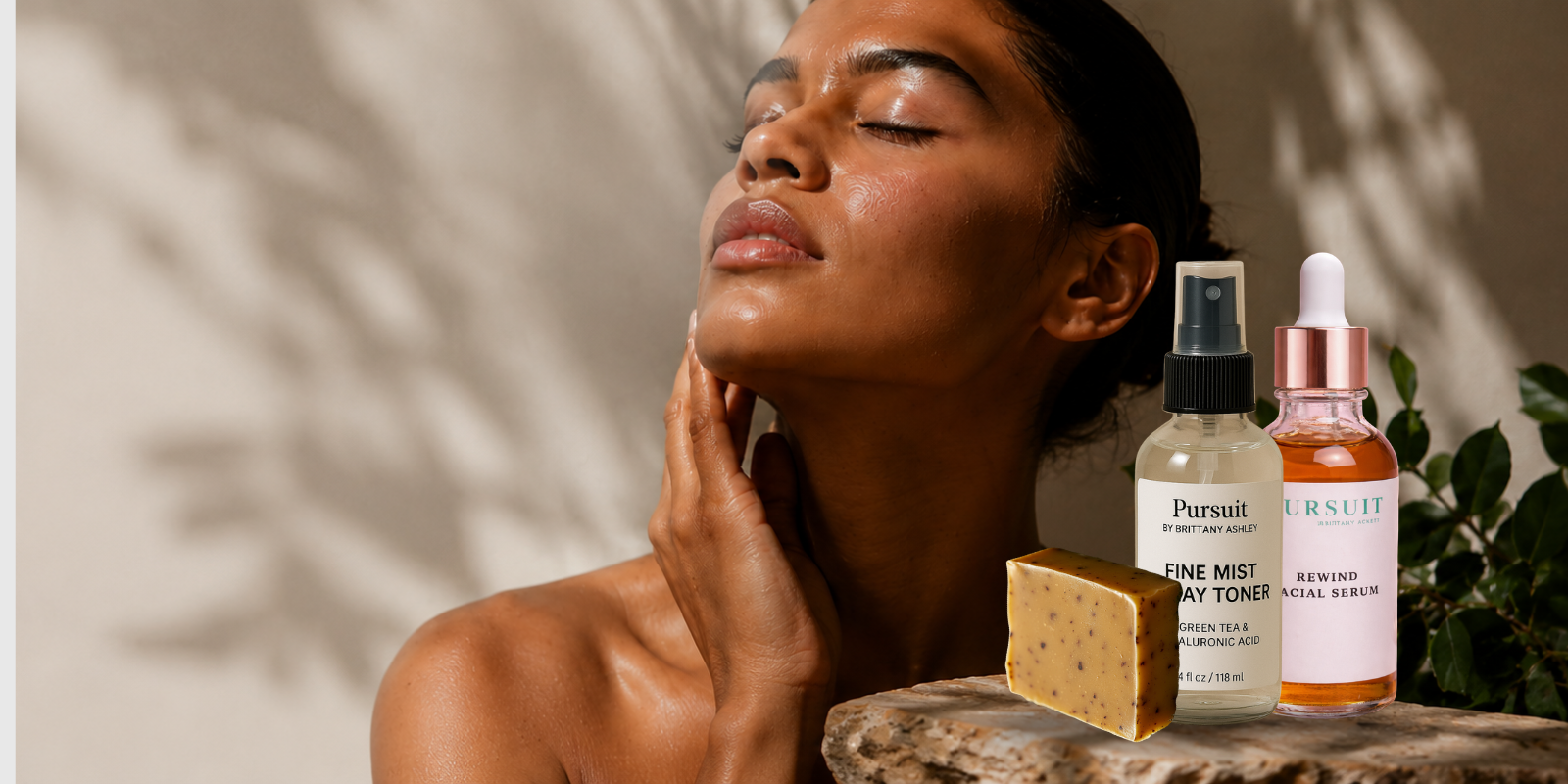 Woman applying skincare product with skincare bottles and a bar of soap on a stone surface.